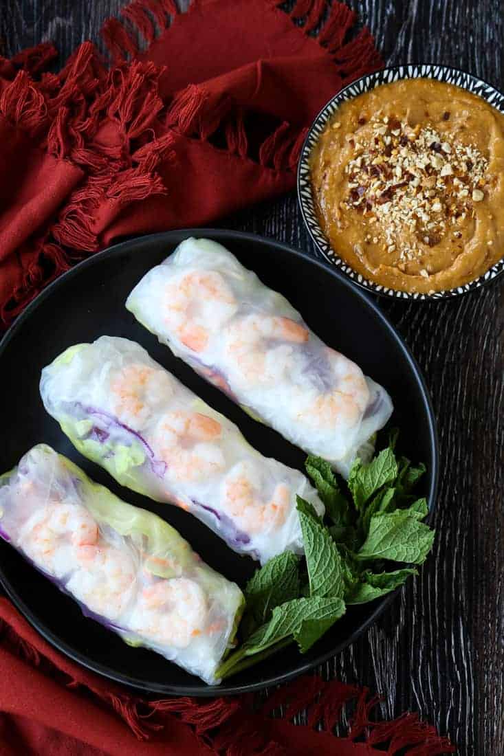 Shrimp spring rolls on a black palate with peanut sauce