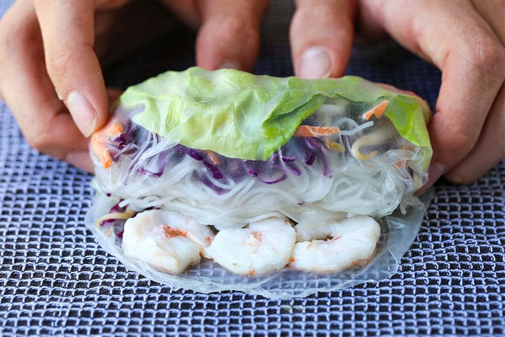 Shrimp Spring Rolls are so light and fresh – making them at home is easier than you think! Serve with our addicting peanut sauce for dipping! rolling up a shrimp spring roll on a towel