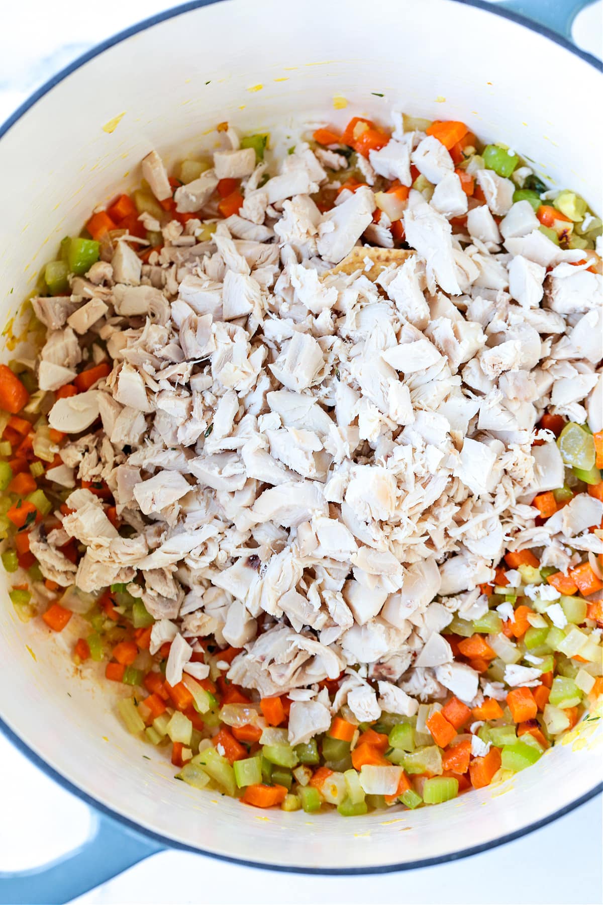 shredded chicken in a pot with diced vegetables for making chicken soup