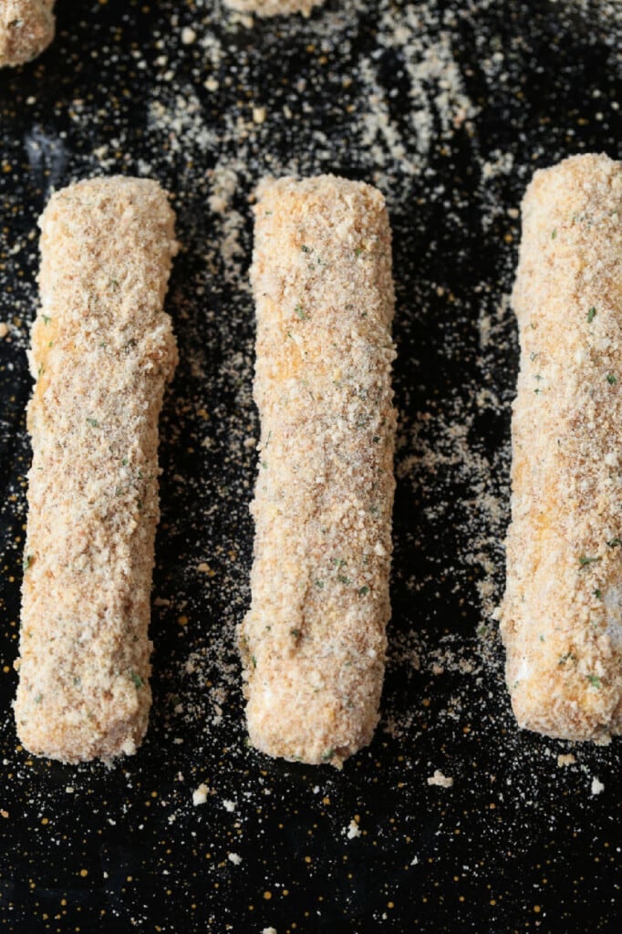 breaded mozzarella sticks on a baking sheet
