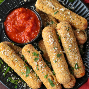 mozzarella sticks on a black plate with sauce