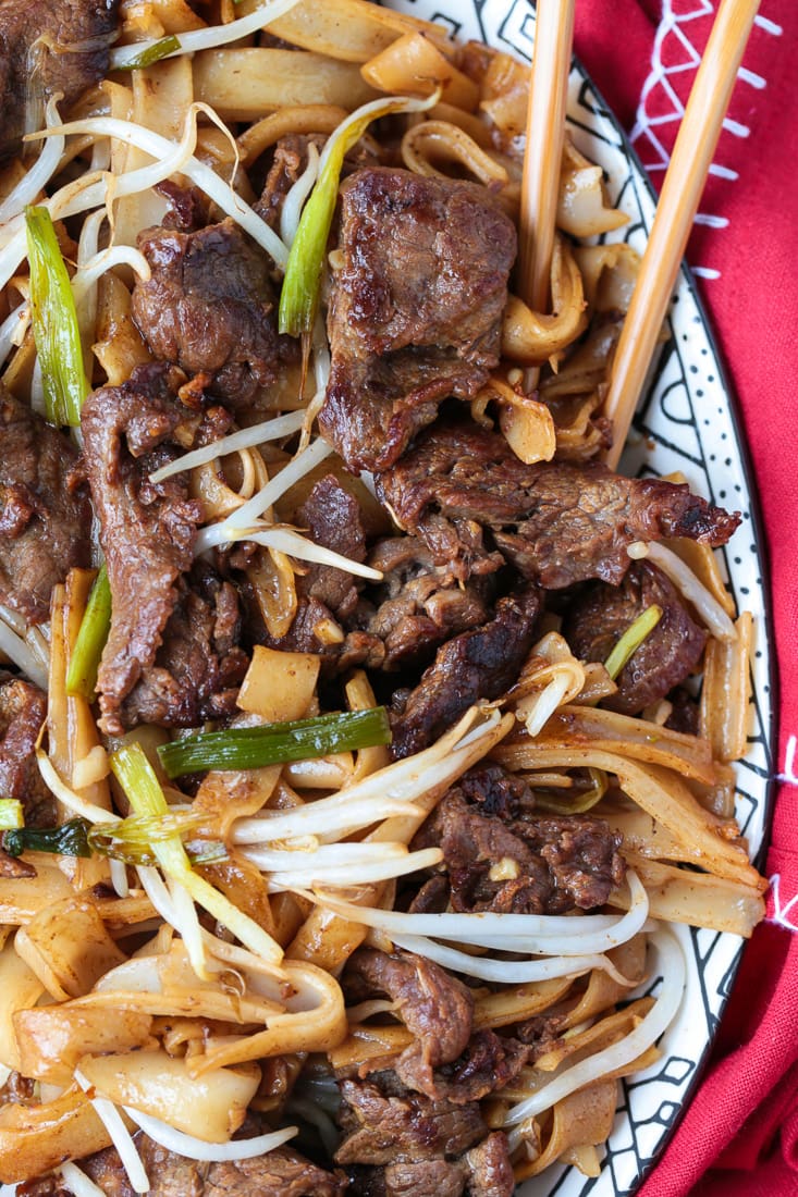 Close up of a serving dish of beef chow fun, with chopsticks