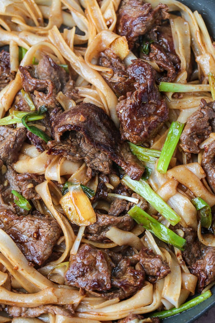 This beef chow fun recipe is a classic Chinese takeout dish, with marinated flank steak, green onions, rice noodles, and bean sprouts. Rice noodles, beef, and scallions stir frying in a pan