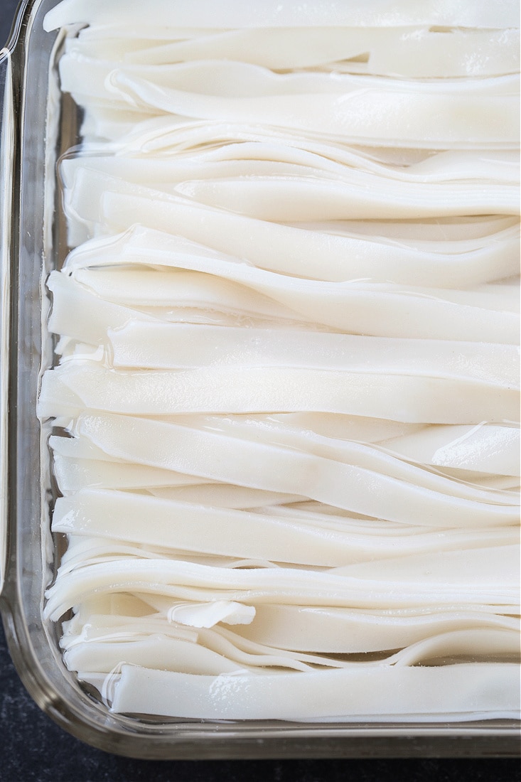 Rice noodles soaking in water in a glass pan
