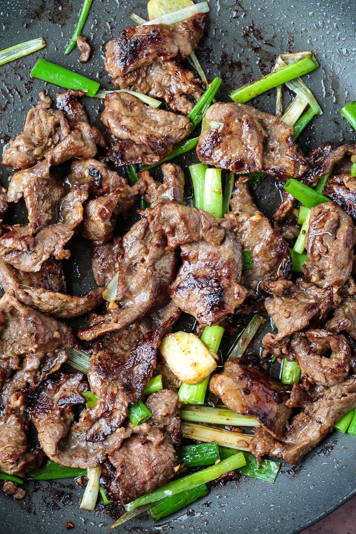 A pan stir-frying slices of flank steak and chunks of scallions.