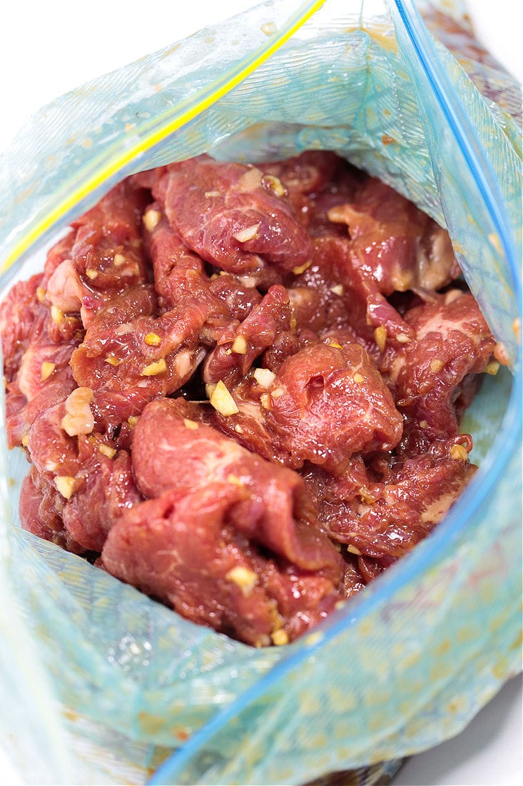 This beef chow fun recipe is a classic Chinese takeout dish, with marinated flank steak, green onions, rice noodles, and bean sprouts. An unsealed ziplock bag with strips of flank steak covered in garlic and marinade.