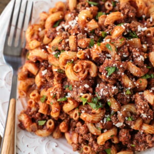 A plate of beefaroni topped with parsley and parmesan, with a fork on the plate