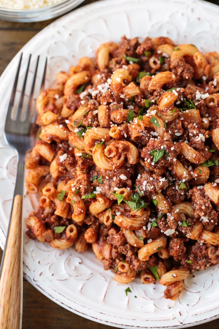 A plate of beefaroni topped with parsley and parmesan, with a fork on the plate