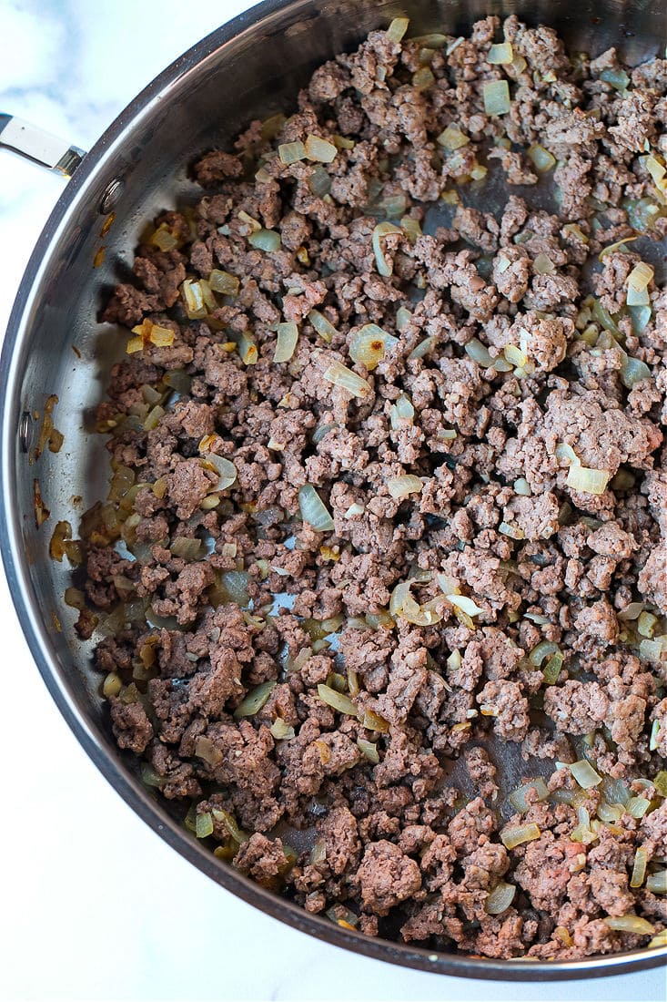 Ground beef cooking in a pan with diced onions and garlic