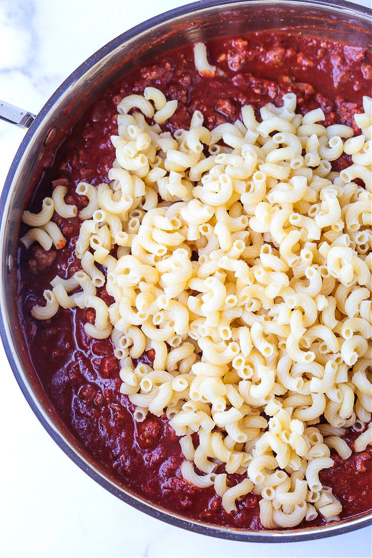 Cooked elbow macaroni on top of tomato and beef sauce in a pan