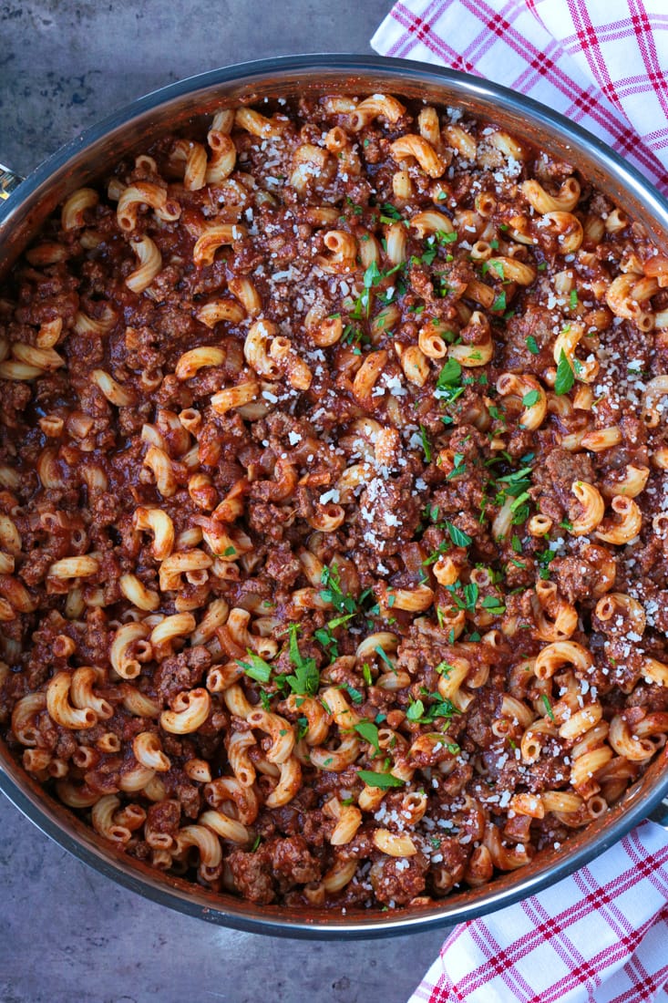 A serving bowl of beefaroni, topped with parmesan cheese and parsley
