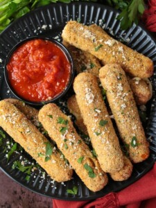 mozzarella sticks on a black plate with sauce