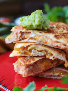 A stack of chicken quesadilla triangles, with a dollop of guacamole on top