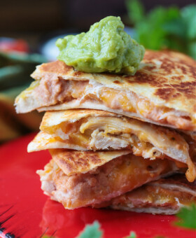 A stack of chicken quesadilla triangles, with a dollop of guacamole on top