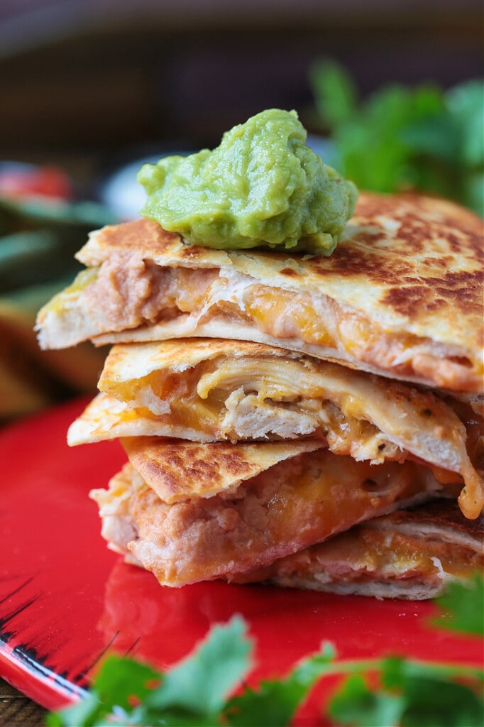 A stack of chicken quesadilla triangles, with a dollop of guacamole on top