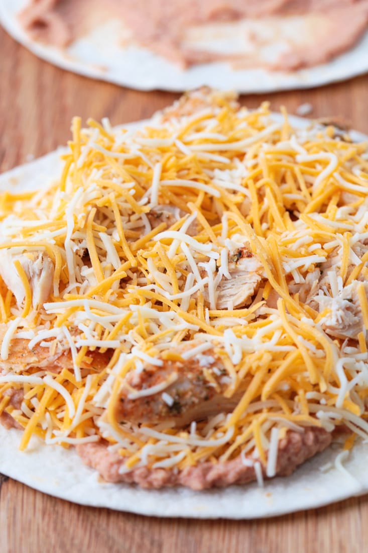 A tortilla with beans, cheese, chicken, and more beans on it