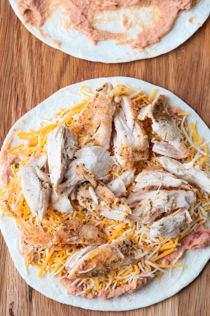A tortilla topped with beans, cheese, and chicken