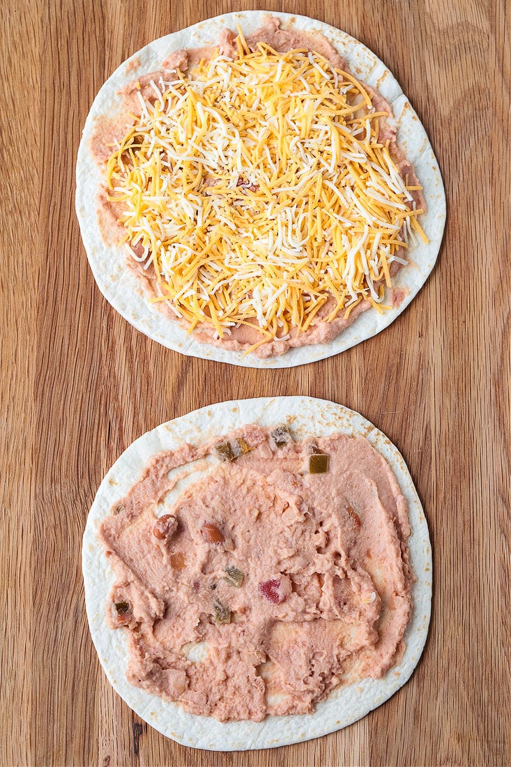 A tortilla covered in refried beans next to a tortilla covered in refried beans and shredded cheese