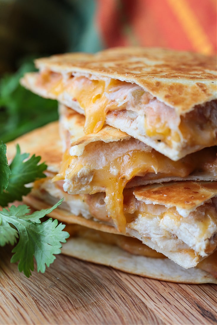 Close up of a stack of chicken quesadilla triangles, next to cilantro