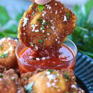 dipping a fried ravioli into marinara sauce