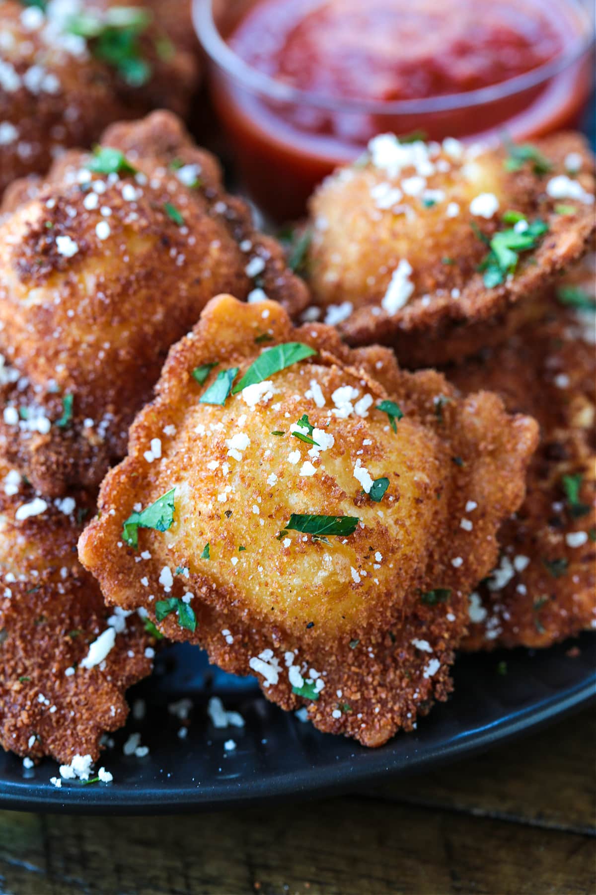 Close up of a fried ravioli with parsley and parmesan cheese on it, with more ravioli in the background