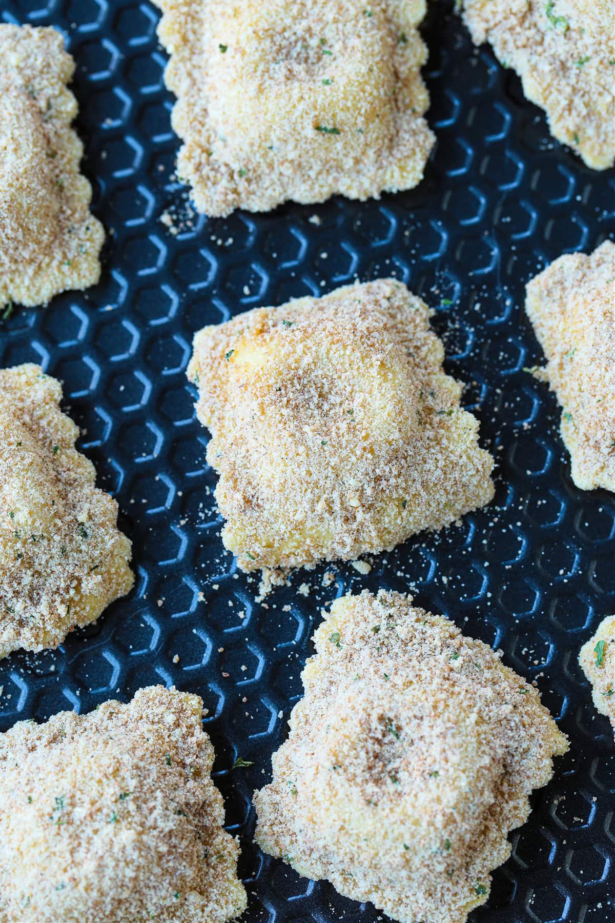 This fried ravioli recipe is crispy on the outside and soft and cheesy on the inside! Dip in marinara sauce for an addicting party appetizer! breaded ravioli on sheet pan