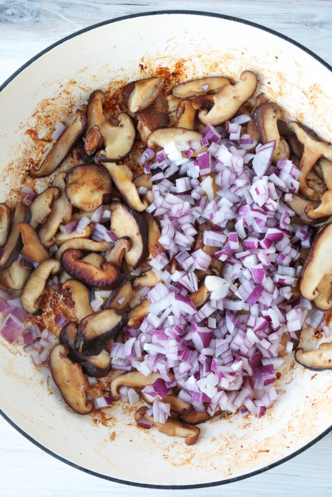 browned mushrooms in a skillet with diced red onion