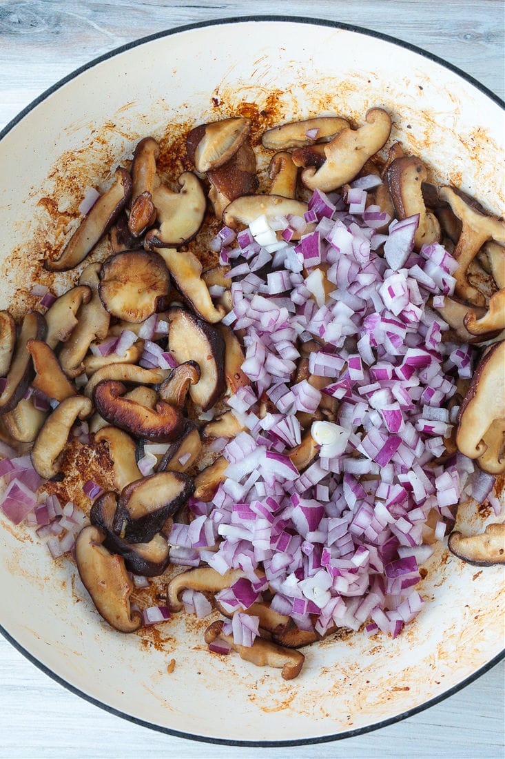 Raw, diced red onion on top of cooked mushroom slices in a pot