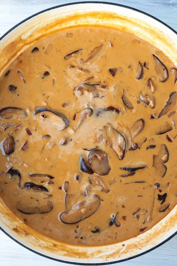 A cream and tomato paste pasta sauce with shiitake mushroom slices in it, cooking in a pot