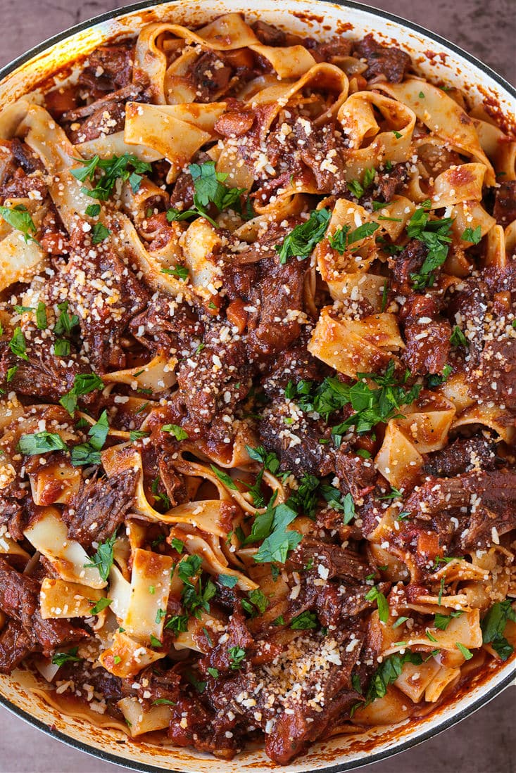 A pot of short rib ragu and pappardelle noodles, topped with parmesan cheese and parsley