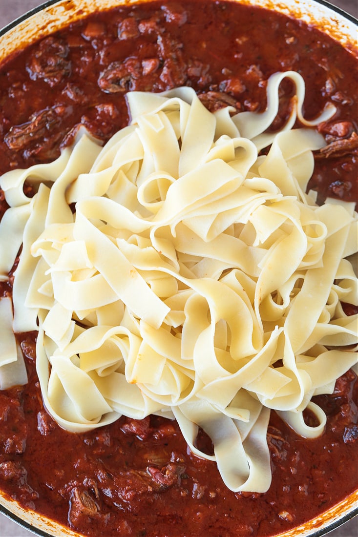 A pot with short rib ragu, with a pile of pappardelle noodles on top