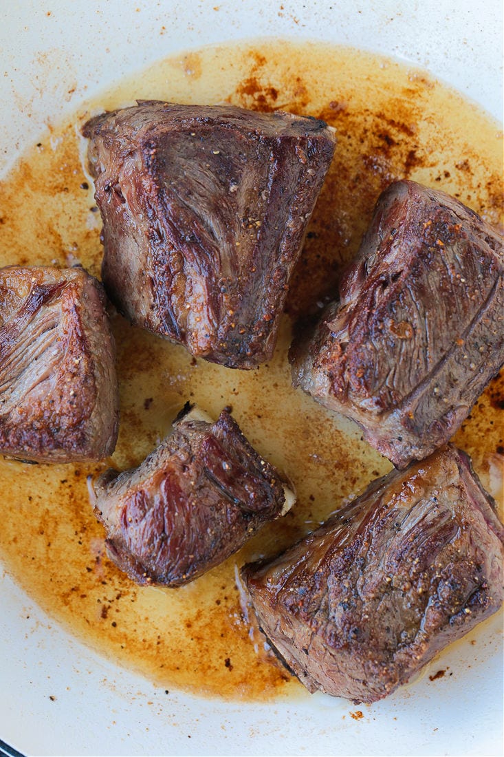 Short ribs braising in a pan, with cooked sides up.