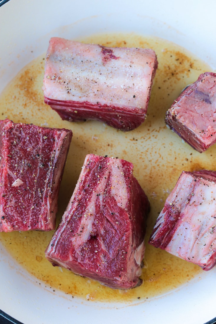 Short ribs searing in a pan, raw side up.