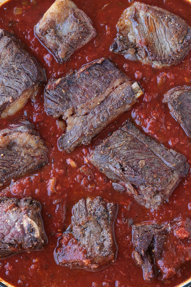 Whole short ribs braising in a tomato sauce.