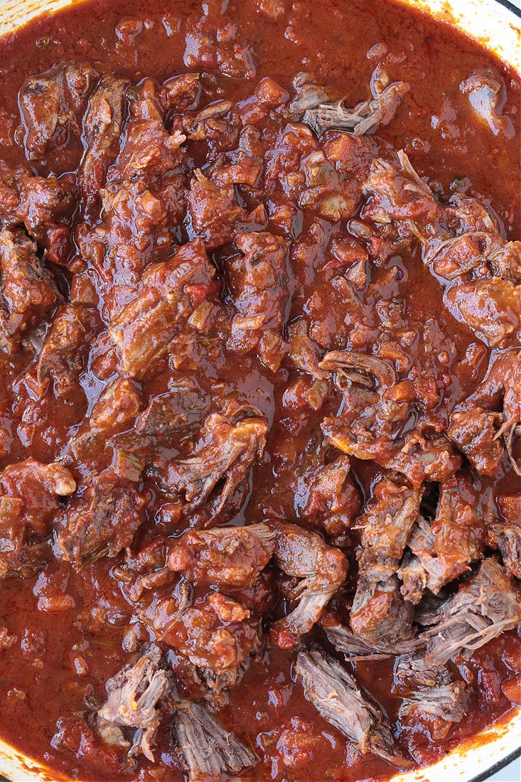 Shredded short ribs cooking in a ragu sauce in a pot.