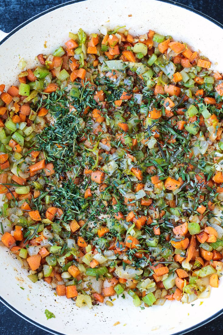 Diced carrots, onions, celery, garlic, rosemary, and thyme cooking in a pot.