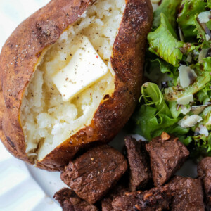 baked potato with butter on plate with salad and steak