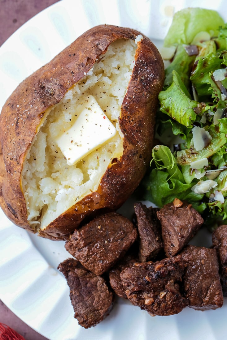 baked potato with butter on plate with salad and steak