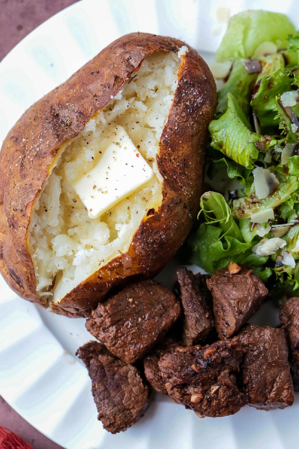 These fluffy Air Fryer Baked Potatoes have the most crispy skin! Free up the oven and let the air fryer do the work for you! baked potato with butter on plate with salad and steak