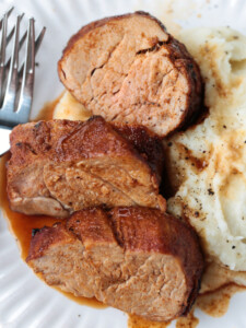 slices of pork on a white plate with mashed potatoes