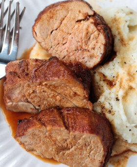 slices of pork on a white plate with mashed potatoes
