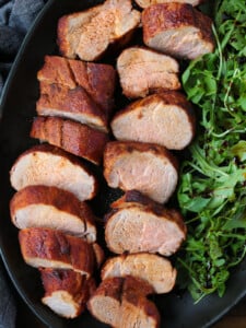 sliced pork on a black platter with arugula