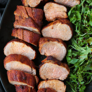 sliced pork on a black platter with arugula