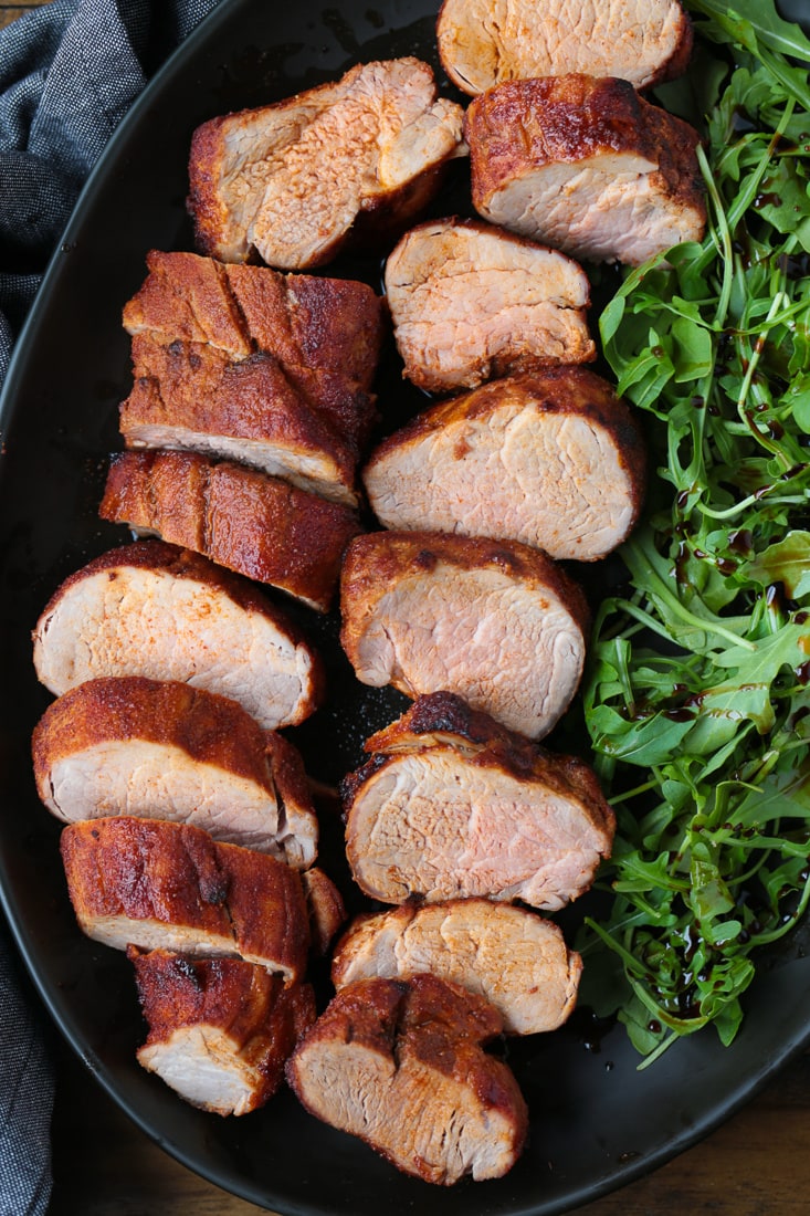 sliced pork on a black platter with arugula