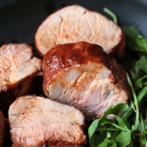 slices of pork tenderloin on black plate with arugula
