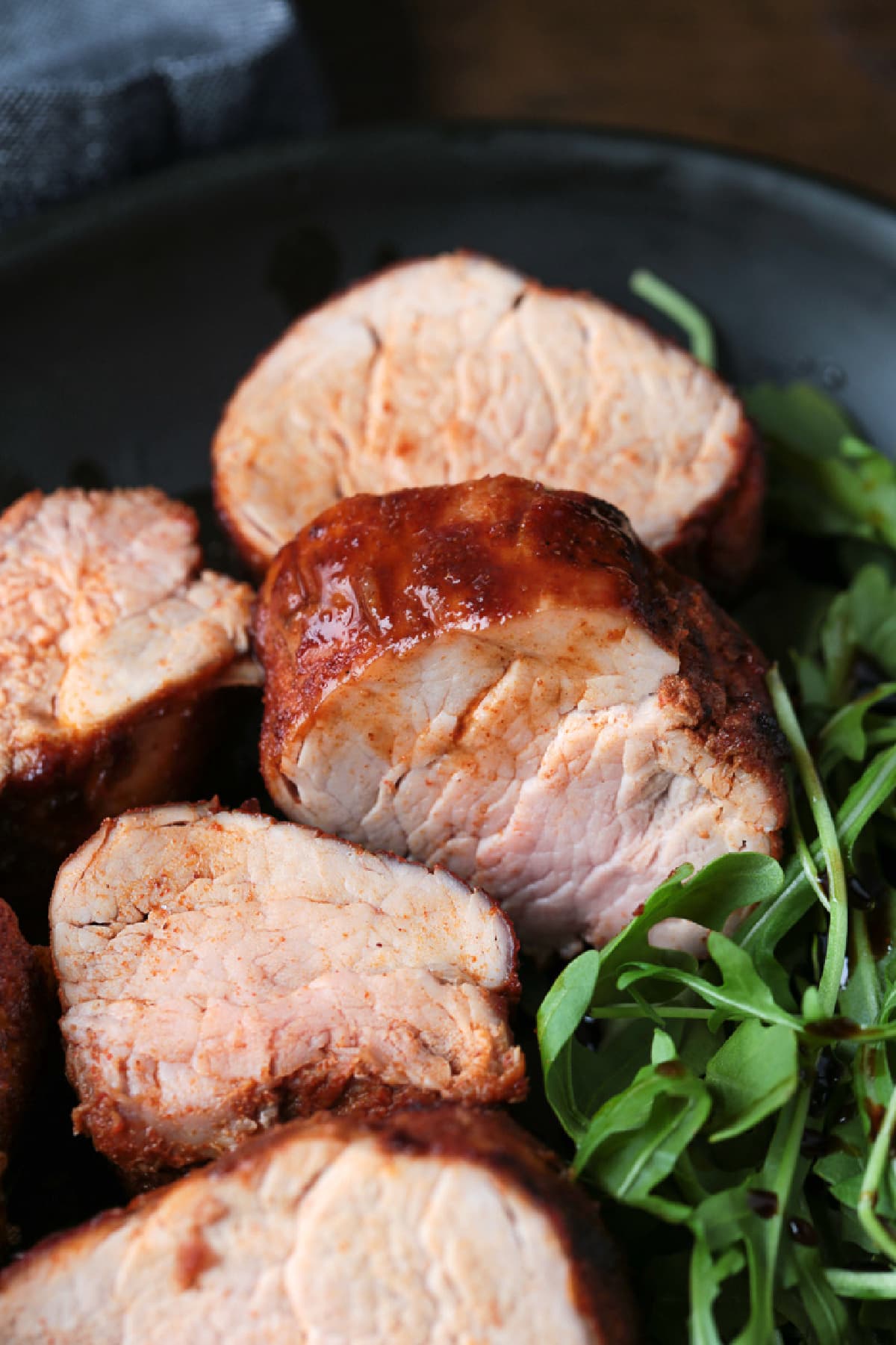Treat your taste buds to a juicy air fryer pork tenderloin! The air fryer helps lock in the juices and gives the pork a golden-brown finish. slices of pork tenderloin on black plate with arugula
