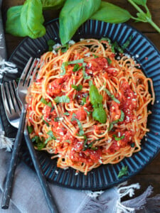 spaghetti on a black plate with fresh basil