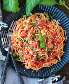 spaghetti on a black plate with fresh basil