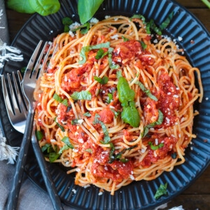 spaghetti on a black plate with fresh basil