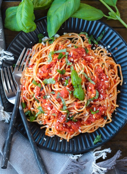 spaghetti on a black plate with fresh basil